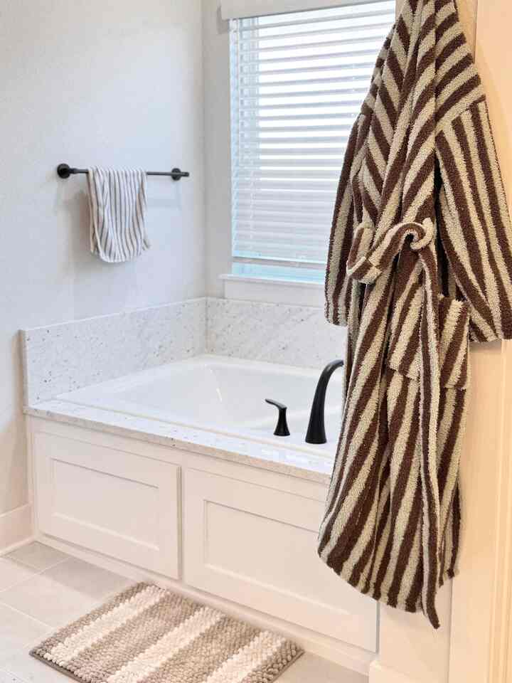 Modern bathroom space featuring white tones with brown striped towel and robe