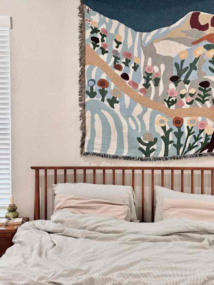 Natural beige wall and wood tone bed frame with striped bedding in a cozy bedroom space