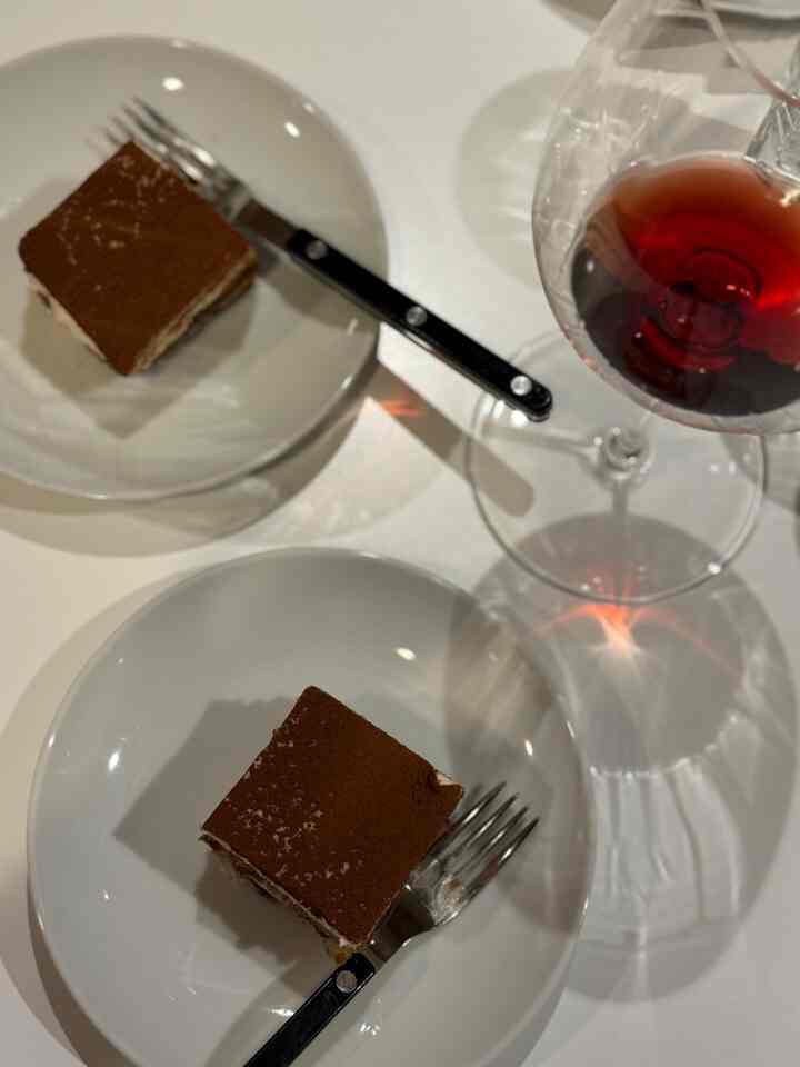 White dining table with two plates of tiramisu and a wine glass, creating a cozy home cafe atmosphere