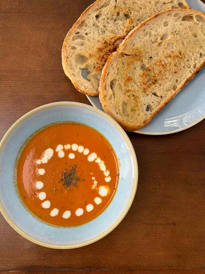 Brown wooden table featuring a plate with toast and a bowl of tomato soup with cream in a kitchen setting
