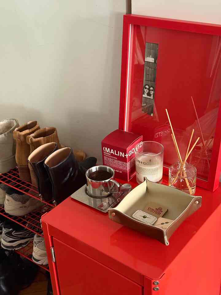 Vibrant red-toned entrance featuring a shoe rack and a red rolling cabinet topped with candles and a diffuser, showcasing simple design