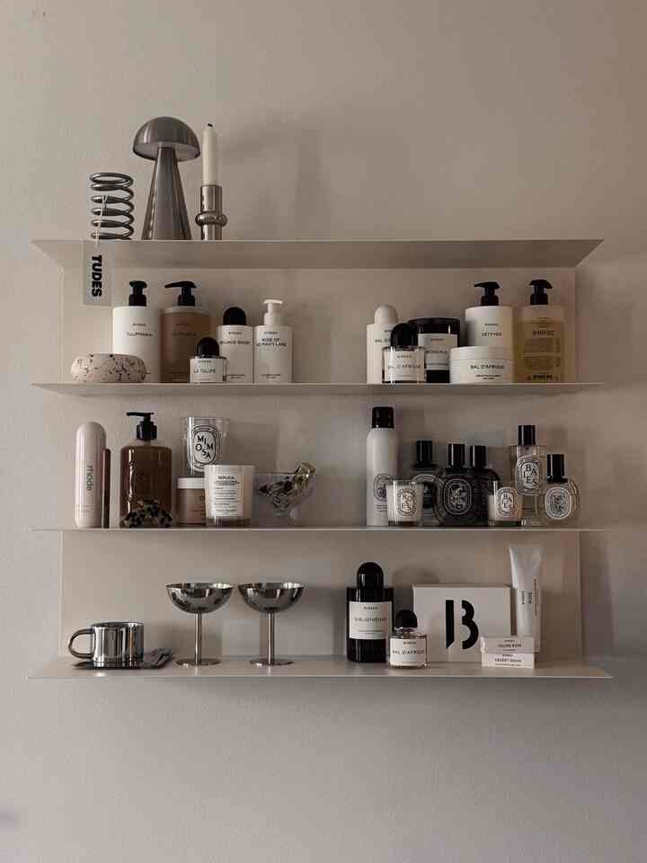 A modern, minimal space with white and silver-tone wall shelves neatly organized with body care and perfume products