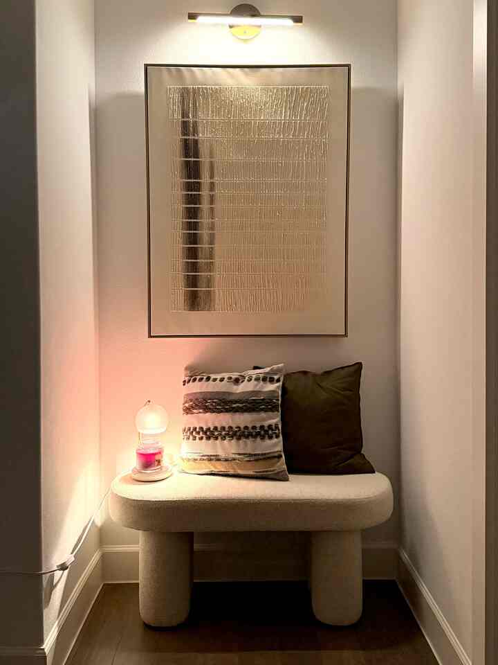 Cozy beige and white tone entrance corner featuring a bench with two cushions and a wall sconce light