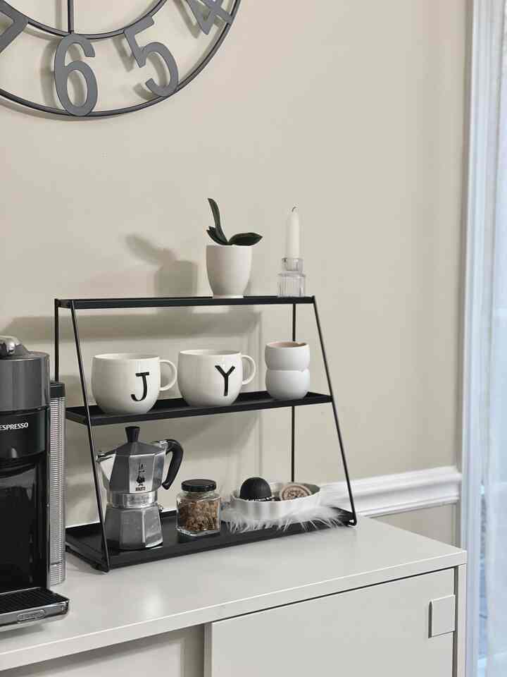 Clean white and black kitchen corner featuring coffee tools and mugs on modern metal shelving