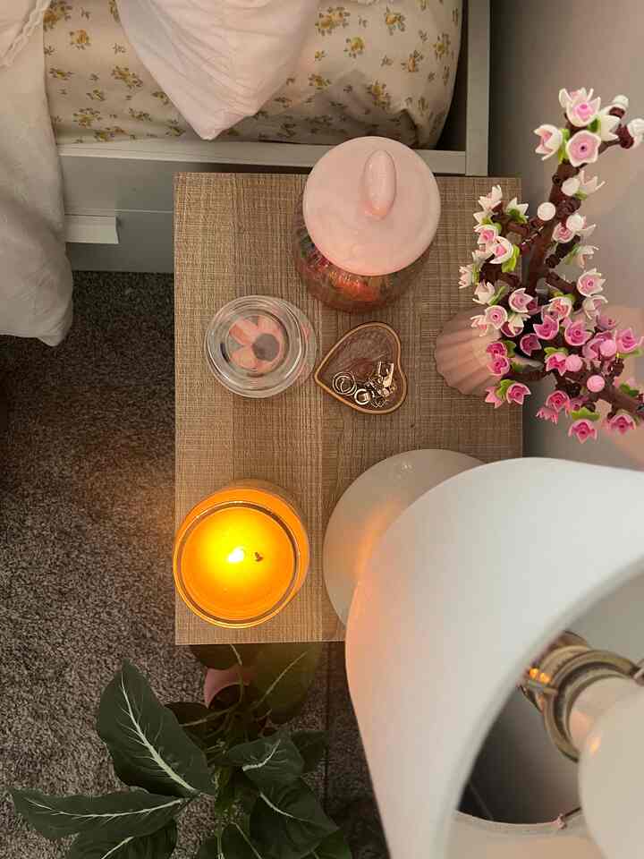 Natural-toned wooden nightstand in a white bedroom featuring a pink vase with floral decor and small accessories