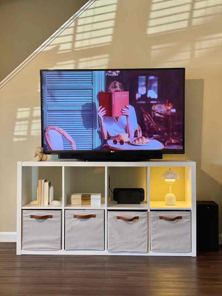 Beige walls and white storage unit in a living room, featuring a large TV and table lamp creating a warm atmosphere