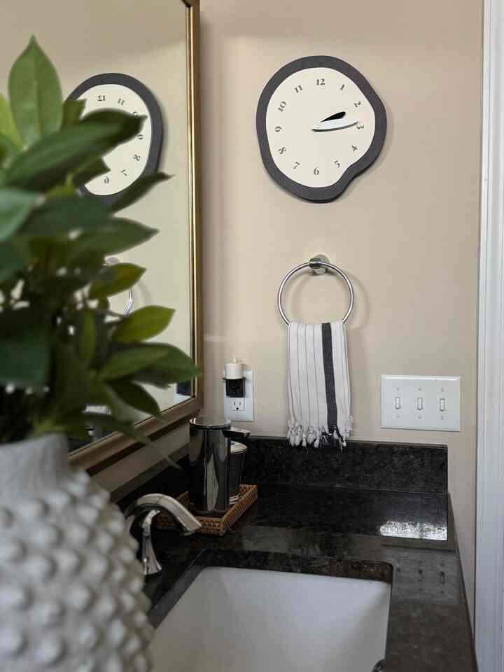 Beige-toned bathroom featuring a quirky shaped wall clock, striped towel, and chrome faucet in a simple, natural setting