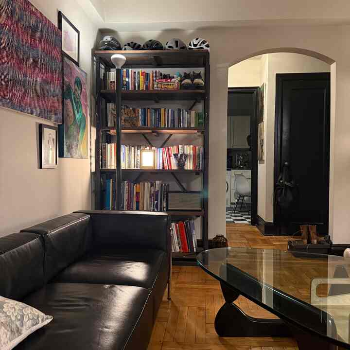 Cozy living room with warm wood-tone parquet floor and black leather sofa, featuring a bookshelf and ambient floor lamp