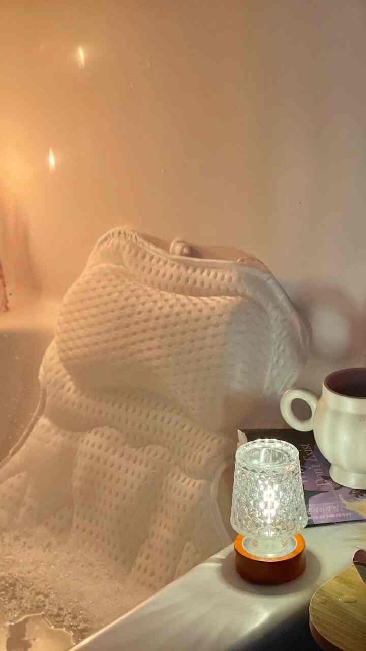 Cozy bathroom scene with warm lighting, white towel draped in bathtub, lit candle, and ceramic mug on edge
