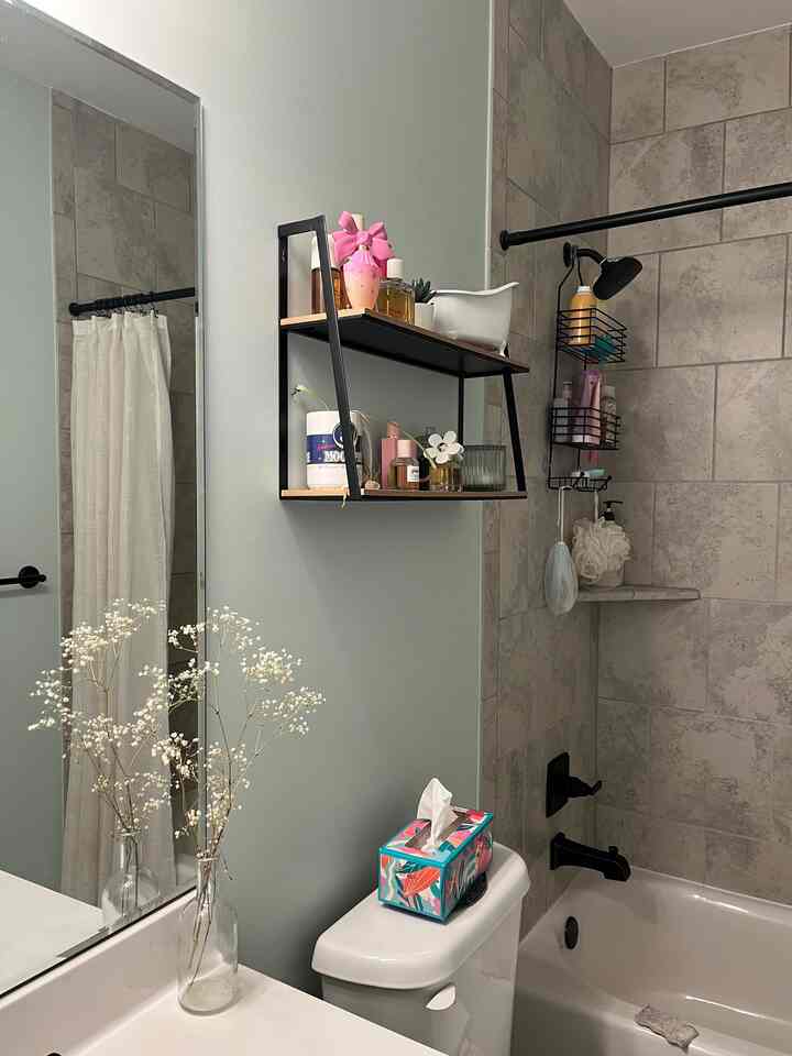 White and gray toned bathroom featuring bathtub, floating shelves, and a vase of flowers creating a neat atmosphere
