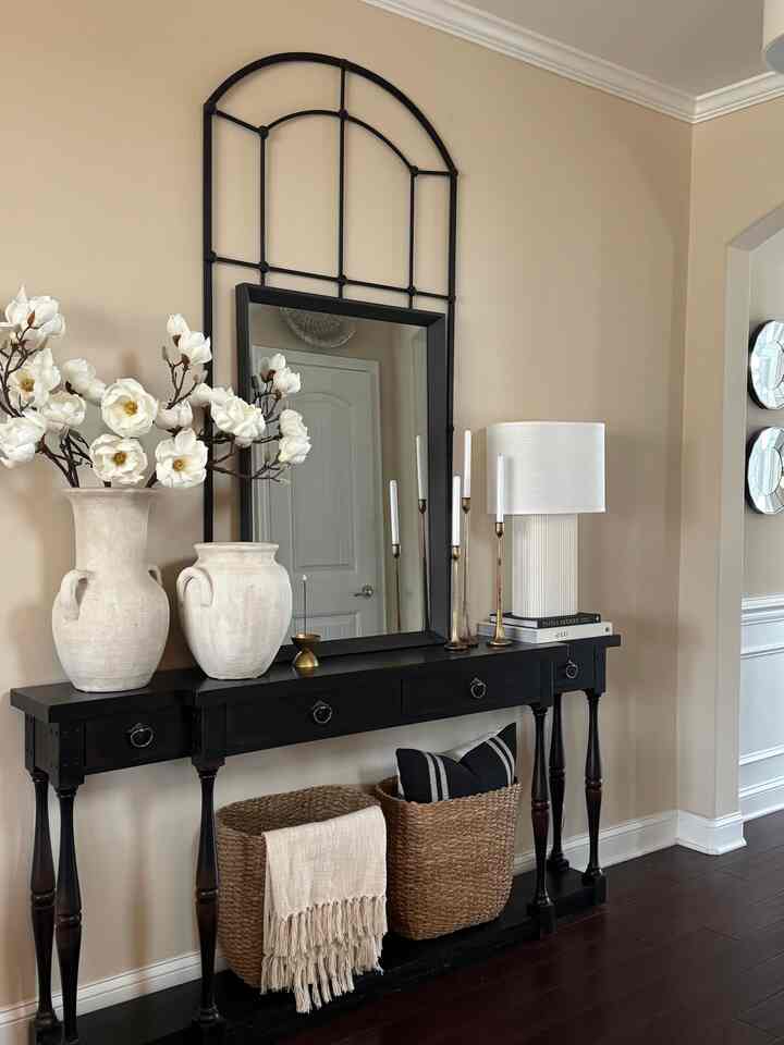 Ivory-toned entrance featuring a black console table adorned with white magnolia flowers and gold candle holders, creating a calm ambiance