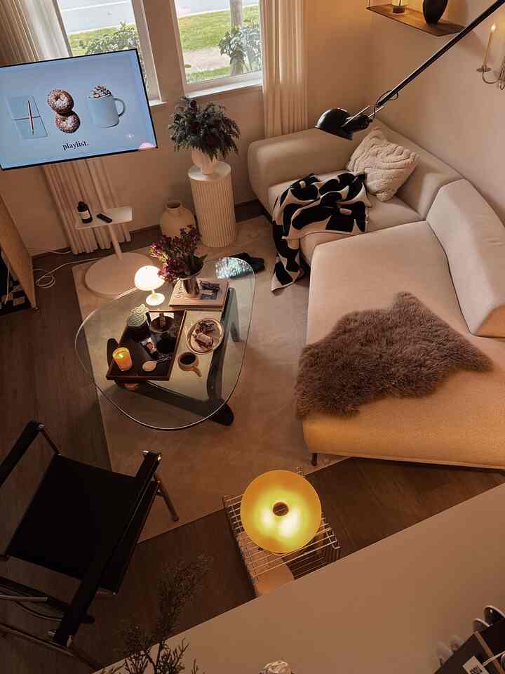 Natural color toned living room with beige sofa and glass coffee table, featuring warm lighting and cozy ambiance