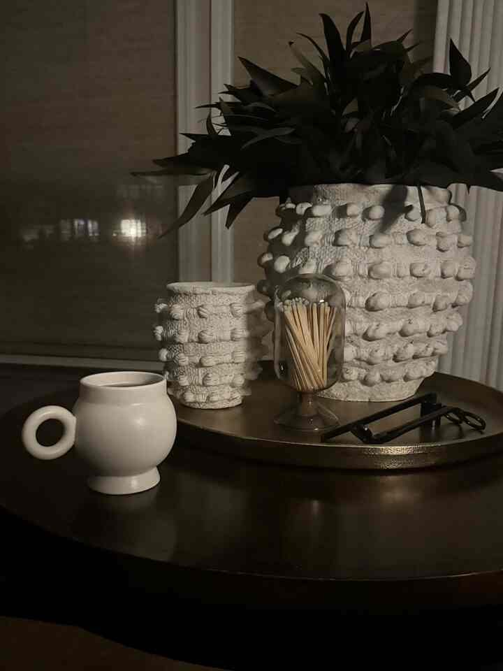 Dark brown round table featuring an ivory mug and textured plant pots in a natural tone home cafe setting