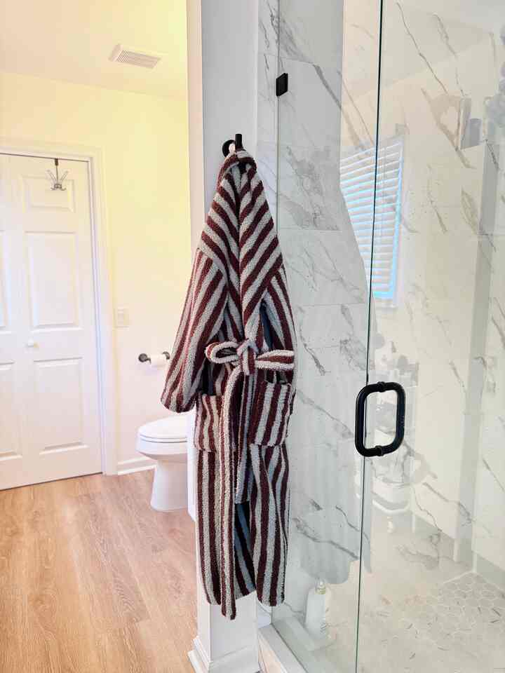 Bathroom with white marble tiles and wood flooring, featuring a plush striped microfiber robe hanging centrally