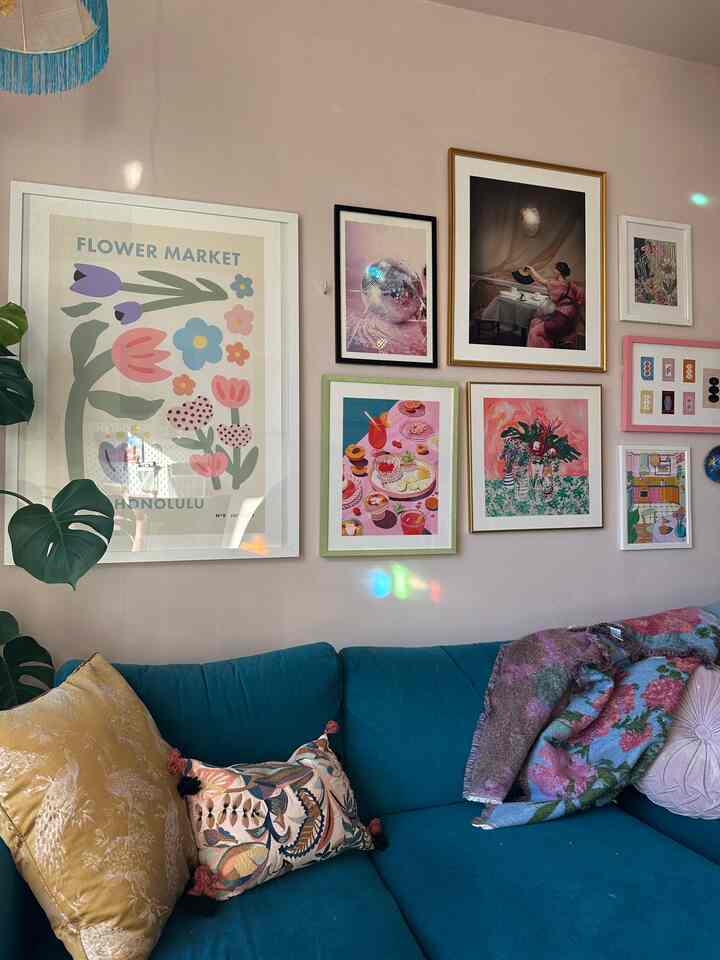 A cozy living room with soft pink walls and a vibrant blue sofa, featuring multiple framed artworks and vintage-style throw blankets