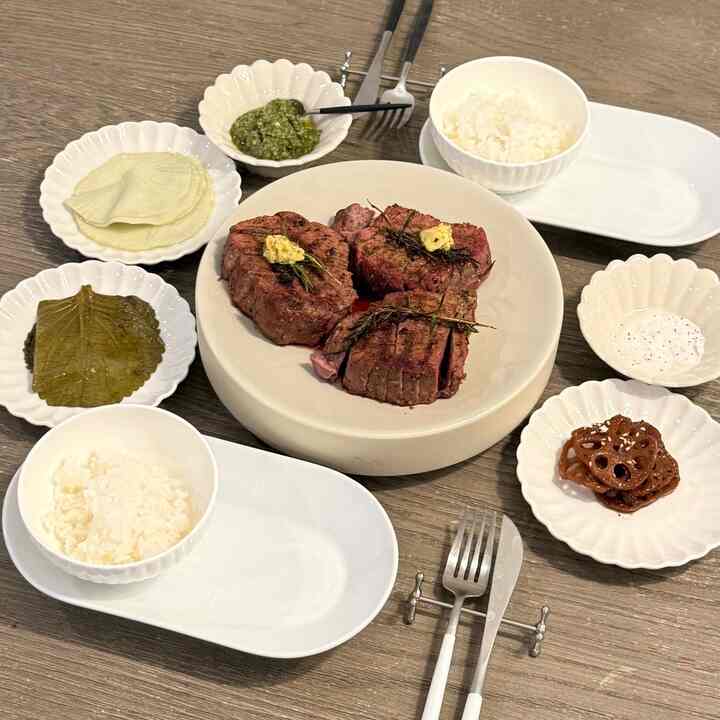Brown wood tone dining table featuring white plates and bowls with steak and rice, creating a cozy meal atmosphere