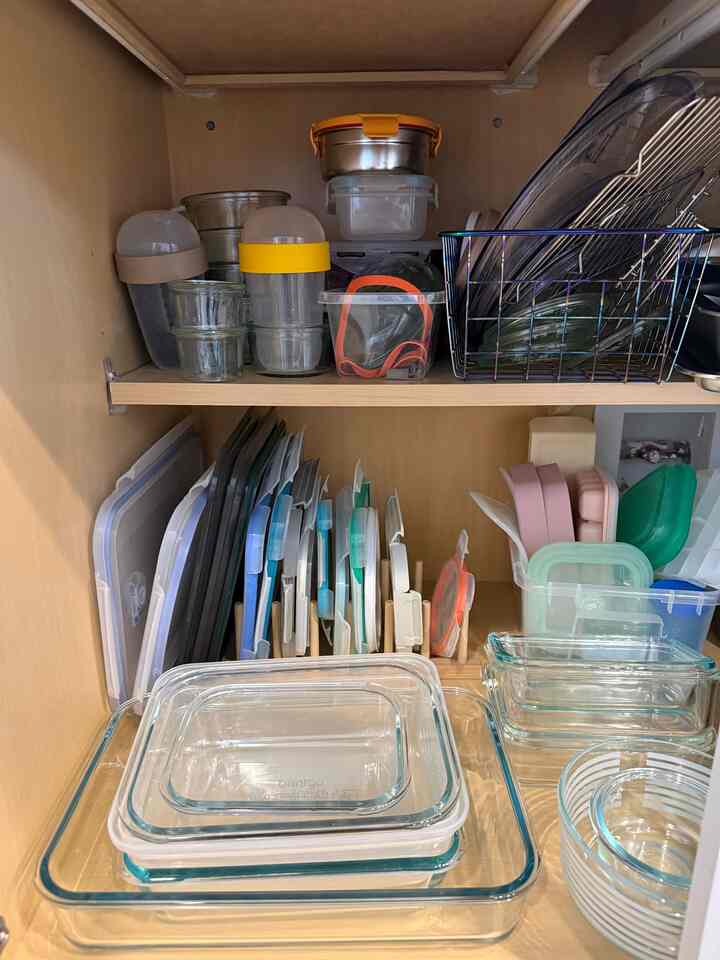 Natural wood-tone cabinet organized with transparent glass and plastic containers, showcasing a tidy kitchen storage space