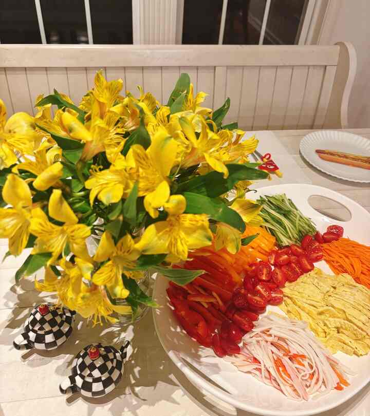 Bright yellow flowers and beige tablecloth in dining room, with colorful ingredients arranged on dining table and checkered salt and pepper shakers