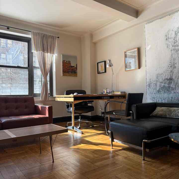 Light brown wooden floor, black and brown leather sofas, desk and office chairs arranged in a bright home office space