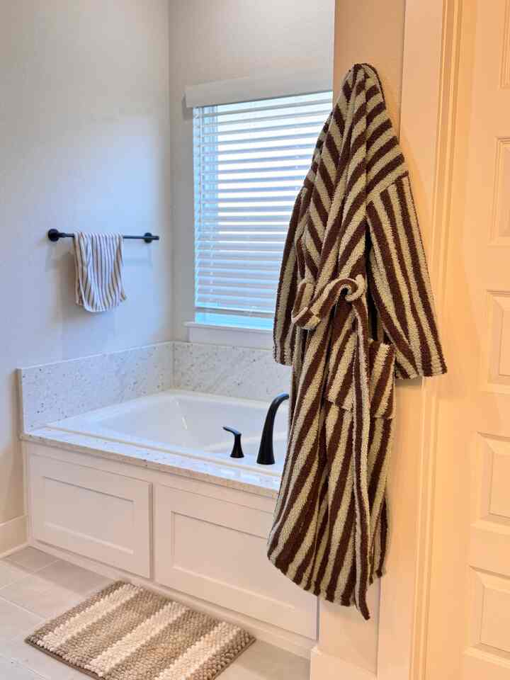 Clean bathroom with white walls and tub, featuring brown striped towels and bath mat