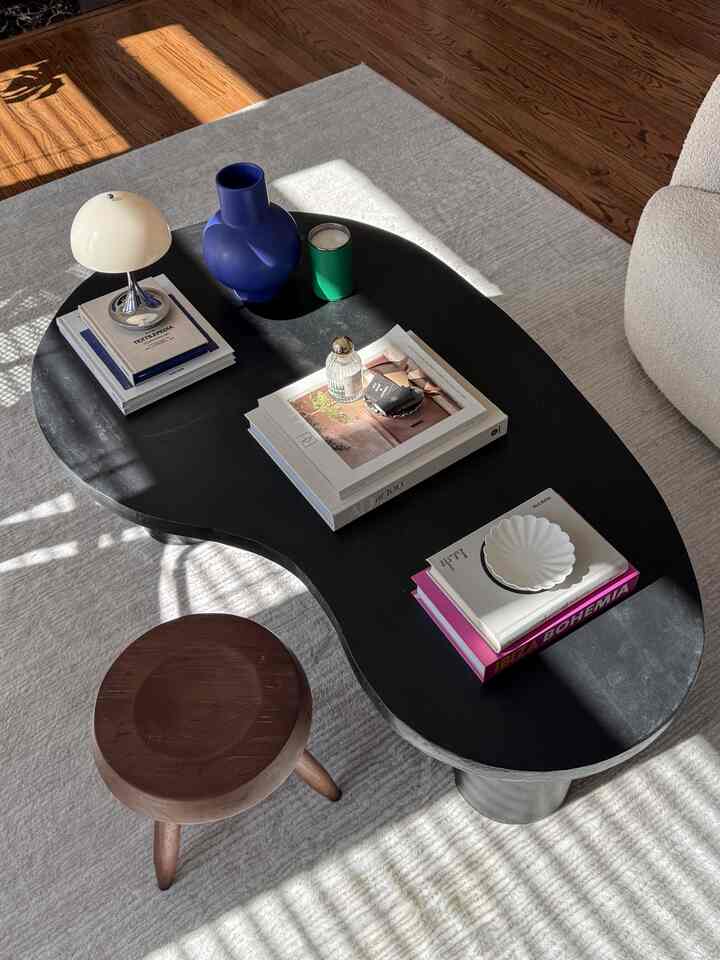 Bright living room featuring a black coffee table and brown stool, decorated with a vase, books, and a lamp on the table, creating a cozy look.