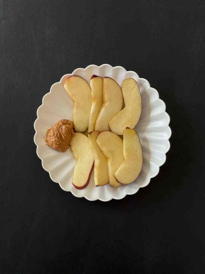 Minimal presentation of sliced apples with peanut butter on a white plate centered against a black background