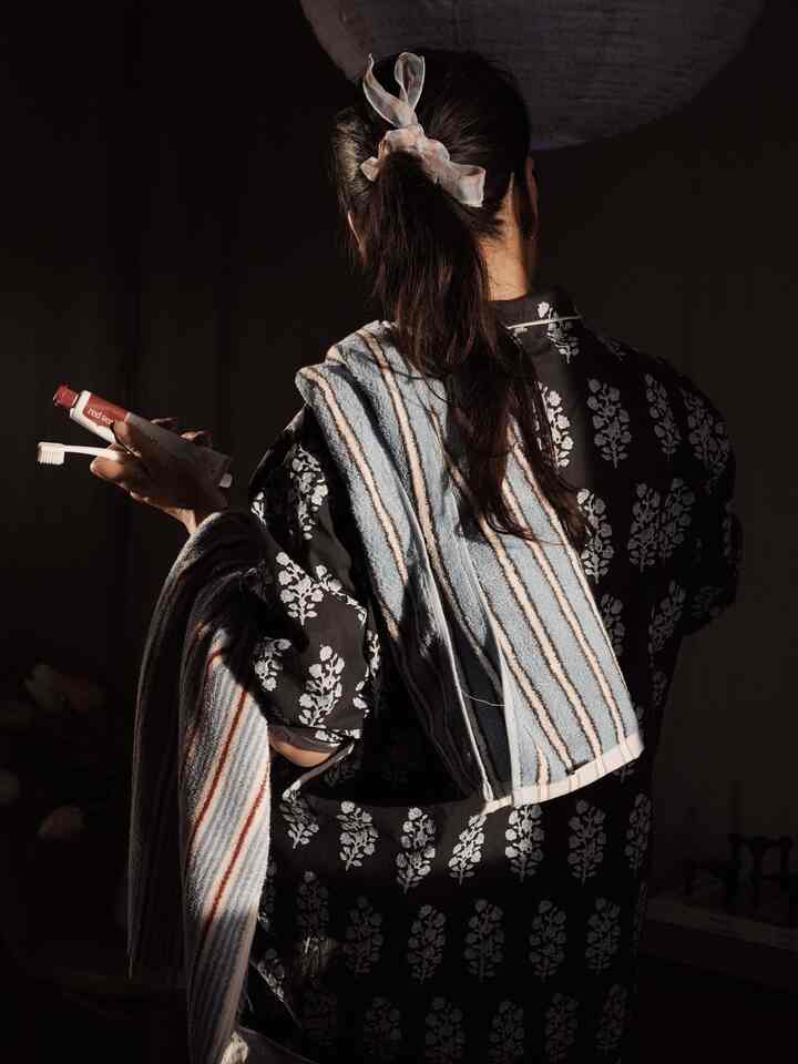 Bathroom scene with a person holding toothbrush and toothpaste, draped in a blue and white striped patterned towel