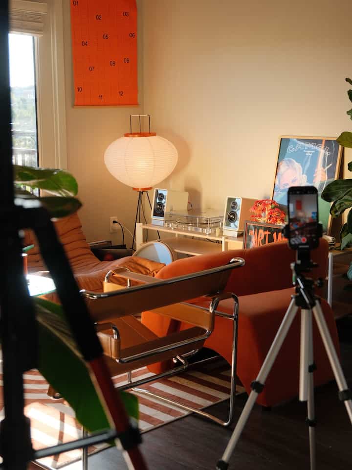 Warm orange-toned living room featuring orange sofa, brown armchairs, floor lamp, and audio equipment with a cozy atmosphere