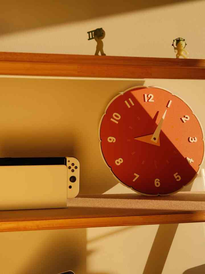 Warm wood tone natural color bookshelf space featuring a prominent red wall clock with minimal decor