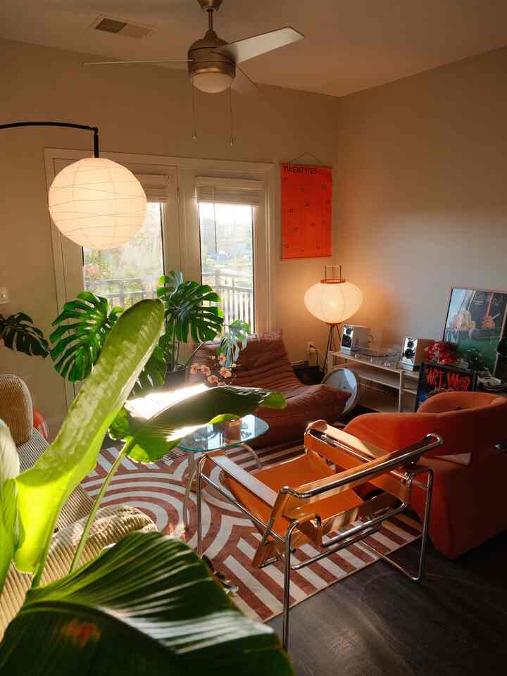Warm orange and brown toned living room featuring vintage chairs and large green plants in a cozy atmosphere