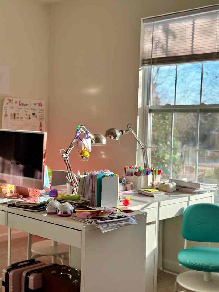 Bright white kids' room featuring white desks and a mint-colored chair by the window with a lively study atmosphere
