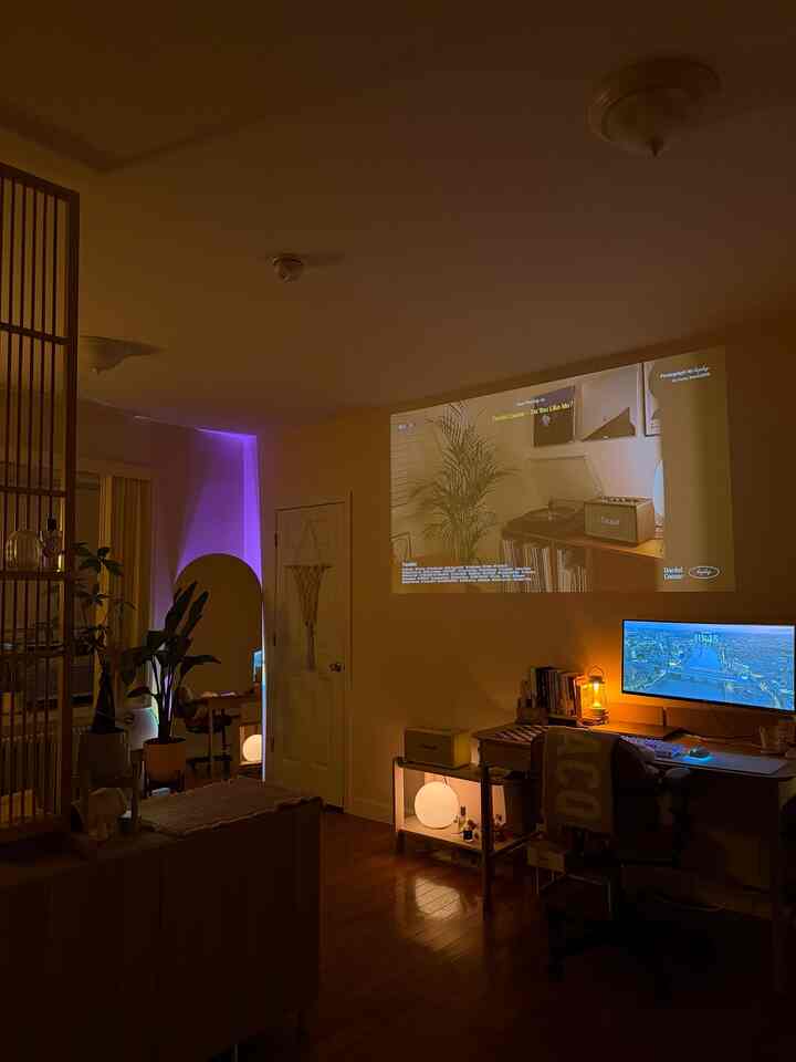 Warm wood-toned modern studio apartment home office with a projector screen and ambient lighting creating a cozy atmosphere