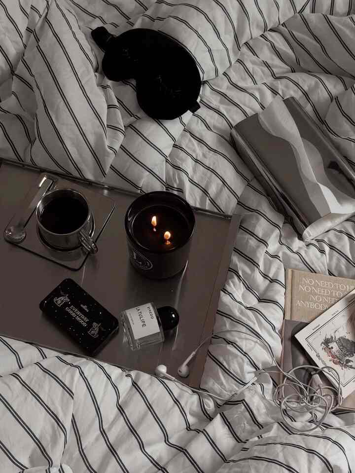 A bedroom with white and black striped bedding featuring a metal tray with a candle and coffee cup, creating a cozy atmosphere