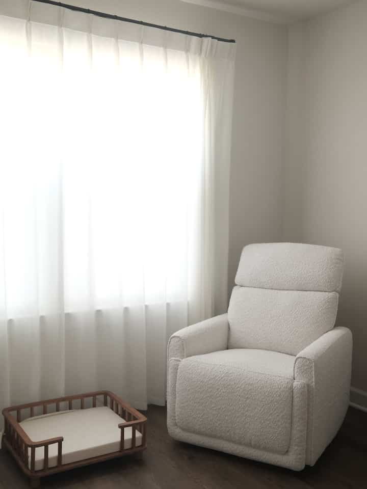 White-toned walls and curtains with a baby glider chair and a wooden-frame dog bed placed in a cozy corner