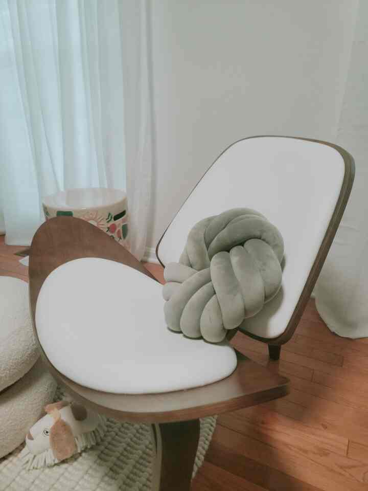 A natural brown wooden armchair with white cushions and a decorative knot pillow in a cozy living room setting