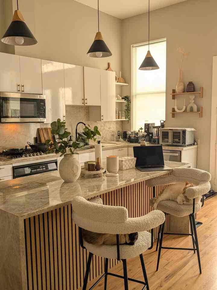 Bright kitchen space with wood-tone flooring and white kitchen island featuring two cats resting on bar stools