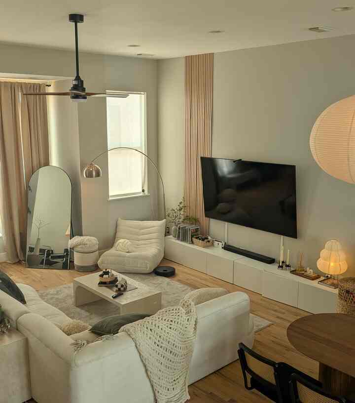 Natural tones and white-dominant living room featuring large sofa, TV stand, and floor lamp with cozy ambiance