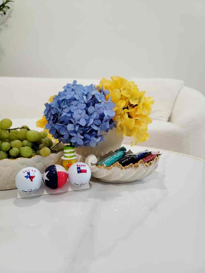 Cozy space with white walls and sofa featuring table decor with gold-edged dish and yellow and blue flowers on a table