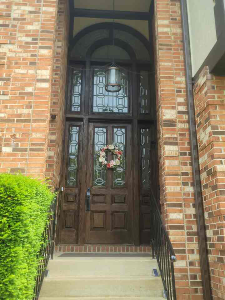 Brown wooden entrance door framed by red brick walls with a floral wreath, classic exterior facade