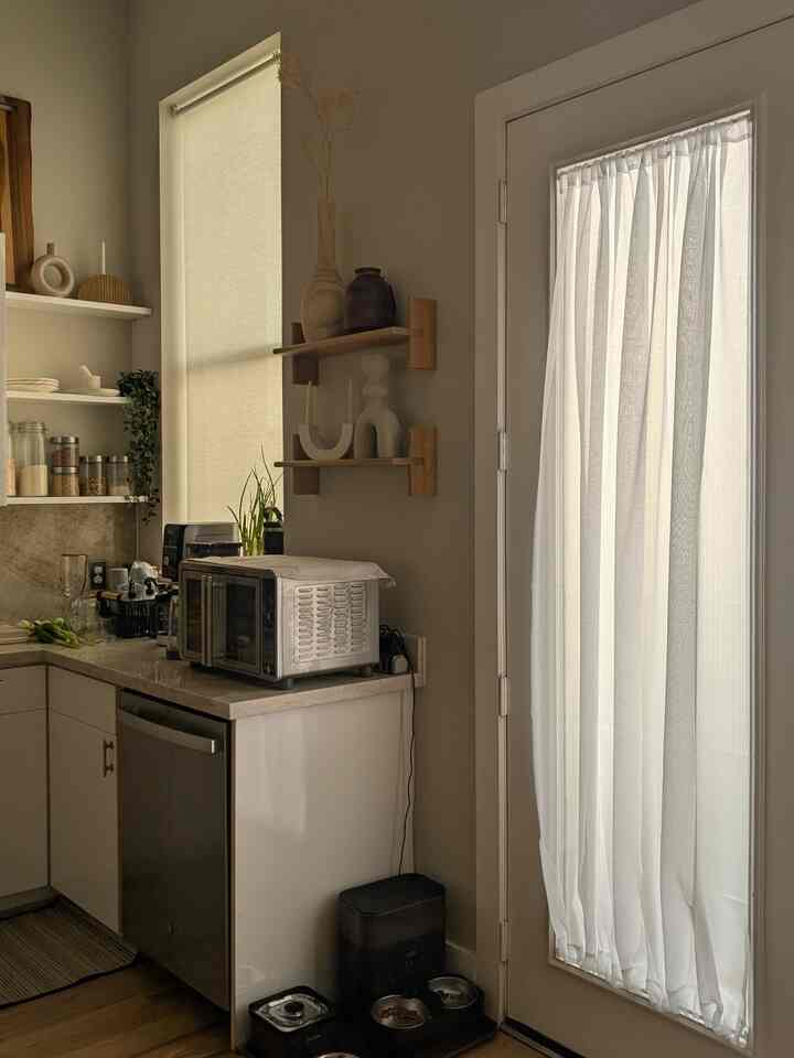 Warm natural tones and white kitchen featuring cat food bowls and a white mesh curtain, creating a cozy atmosphere