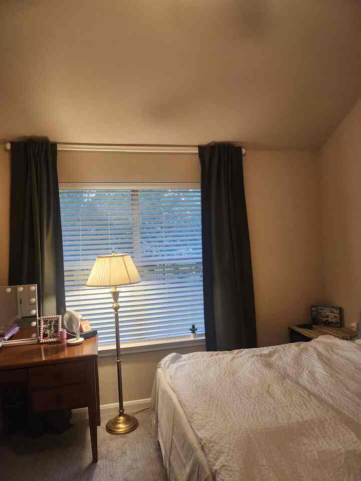 Beige and khaki toned bedroom featuring blackout curtains and blinds on the window with a floor lamp, creating a cozy atmosphere