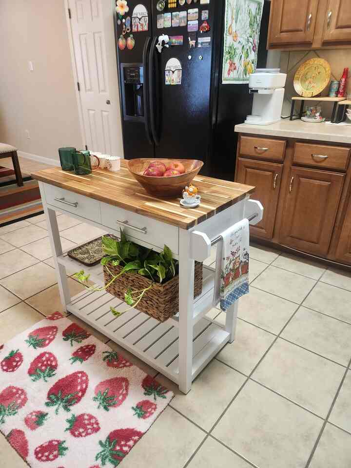 White and wood-toned kitchen space featuring a central kitchen cart and a strawberry-patterned bath mat, creating a cozy atmosphere