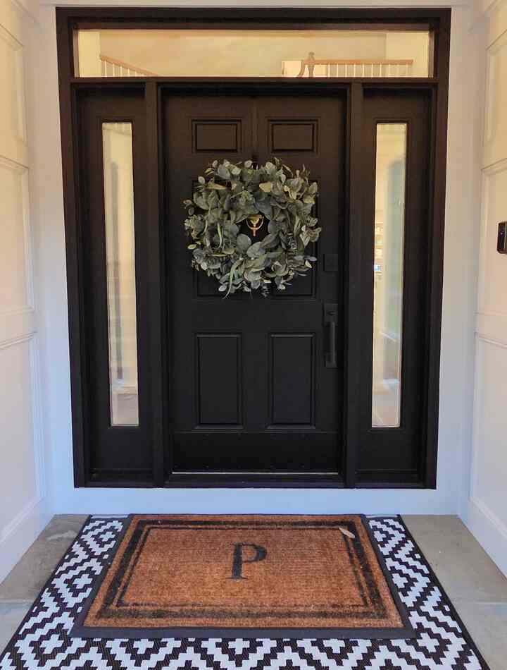 Black door with natural green wreath and brown coir mat at a clean and welcoming entrance