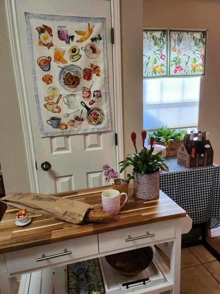 White and blue toned kitchen space featuring pantry door with printed food-themed cloth and gingham check tablecloth on table, cozy atmosphere