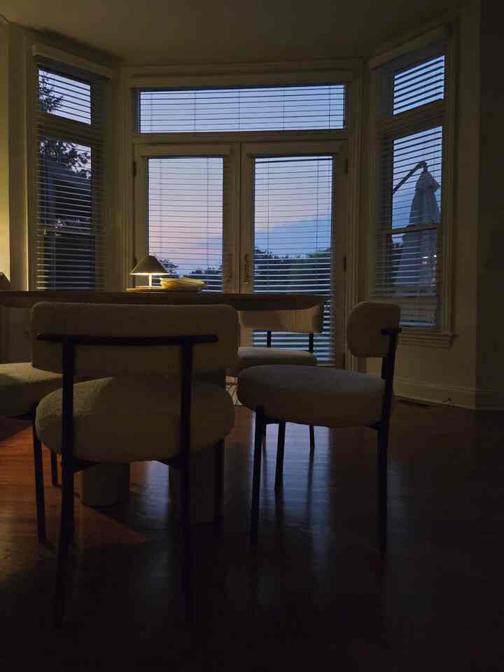 Dining room with earth-toned wooden floor and white boucle dining chairs, evening light creating a calm atmosphere