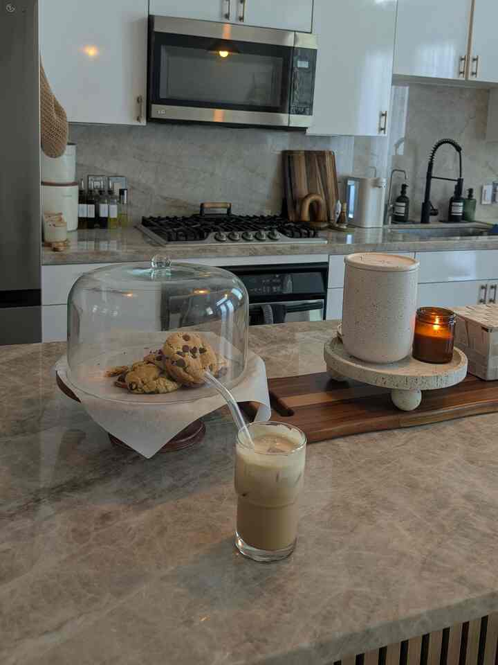 White and brown toned kitchen featuring marble countertops with home cafe style iced coffee, candles, and cookies creating a cozy atmosphere