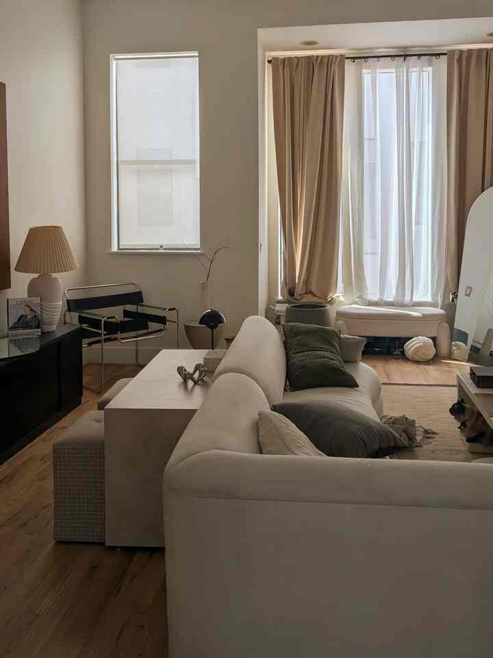 Warm beige natural-colored living room featuring a large sofa with cushions, curtains by windows, creating a peaceful atmosphere