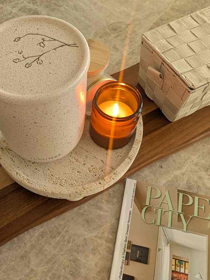 Cozy home cafe setting with a wood tone and beige tray holding a lit candle and decorative items on a marble surface