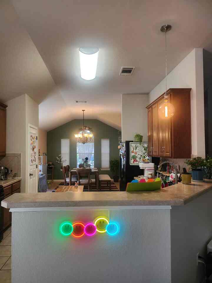 Dining room and kitchen with natural wood tones and green accent wall, featuring a cozy atmosphere highlighted by neon smiley lights on the living space divider