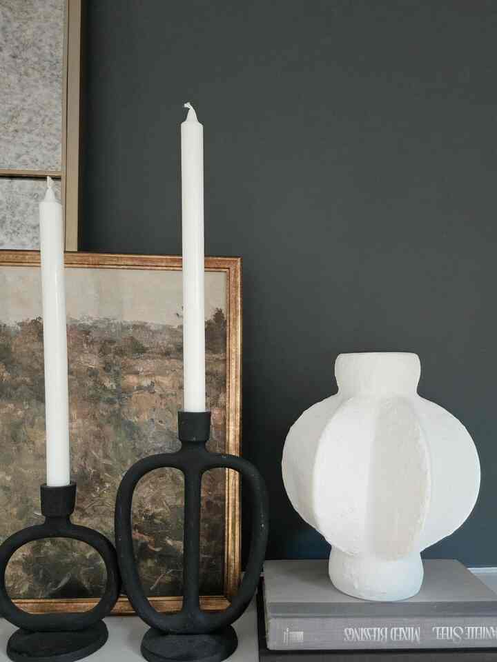 Modern natural objet space featuring white textured stoneware vase and black metal candlesticks against dark gray wall